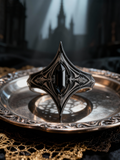 Handcrafted gothic armor onyx silver ring by Kurga Atelier resting on a vintage silver tray inside a gothic cathedral. Dark academia medieval jewelry.