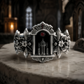 Gothic cathedral reliquary ring in 925 sterling silver with detailed spires and inlaid red gemstone on a stone surface.