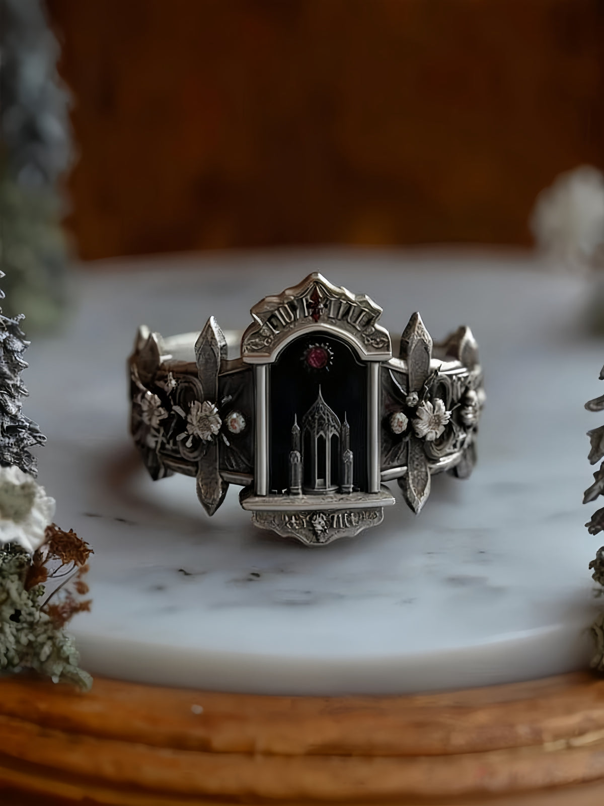 Oxidized sterling silver cathedral ring displayed on a white marble pedestal in a rustic dark academia setup.